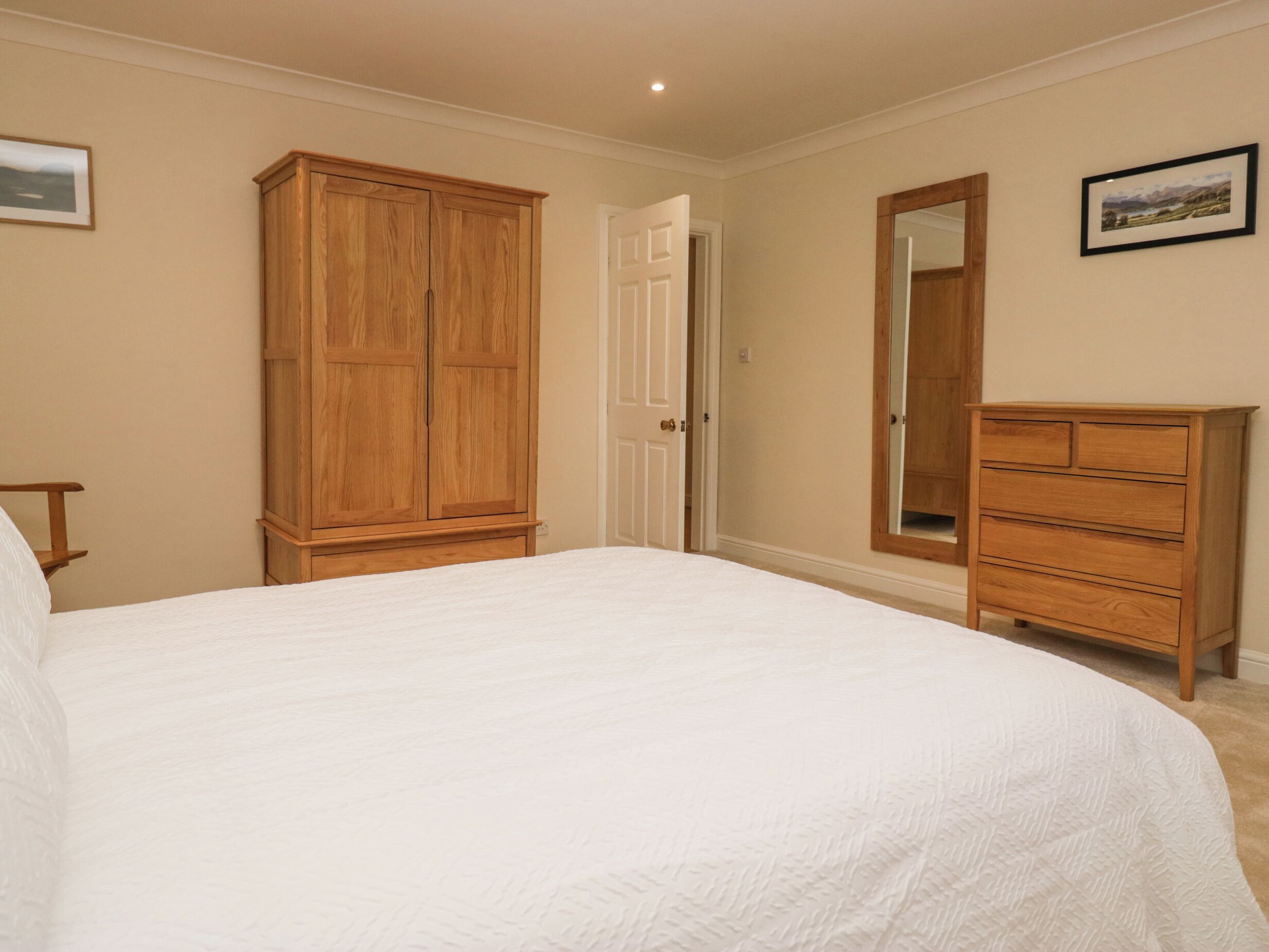 A bedroom with a large bed, wooden wardrobe, and dresser.