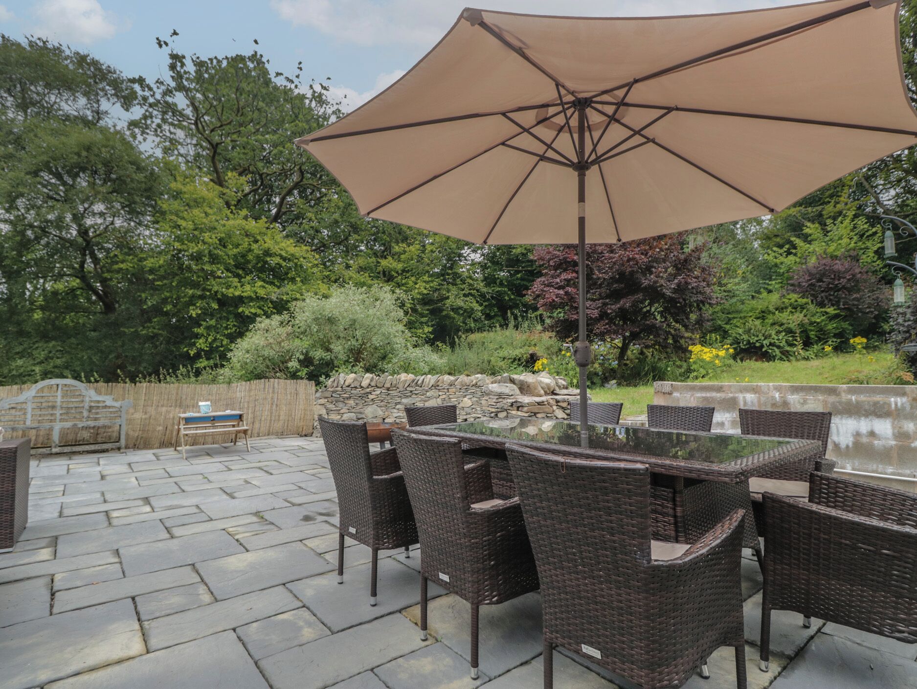 An outdoor patio with a table and chairs, surrounded by stone walls and greenery.
