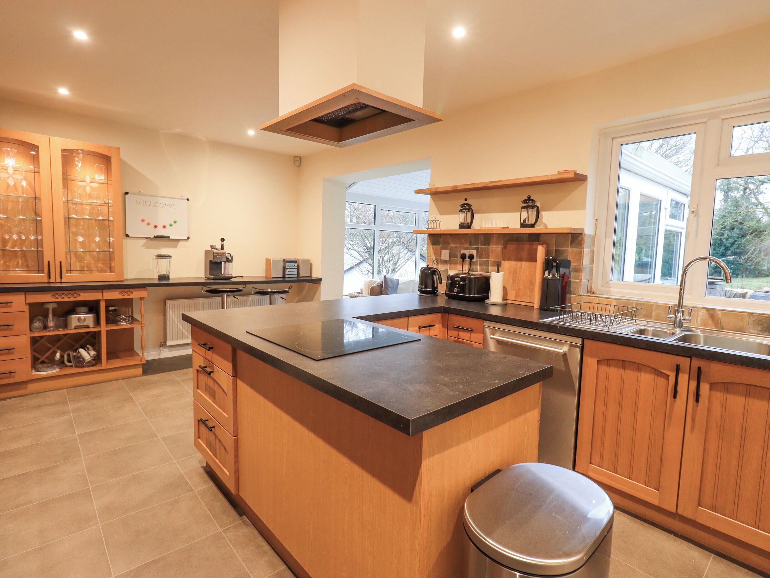 A modern kitchen with wooden cabinets, a central island, and a built-in oven.