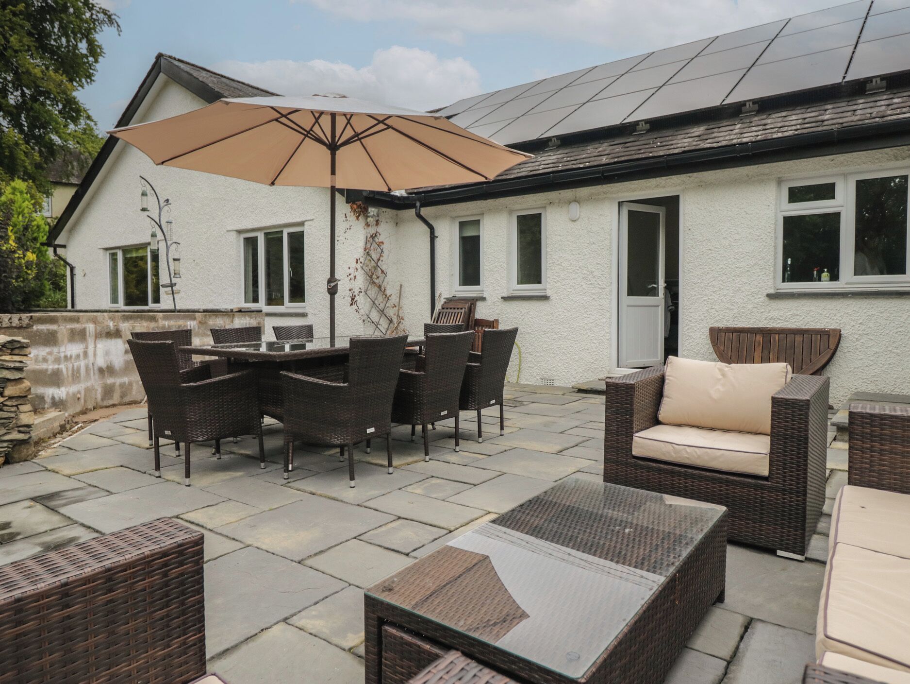 Un espace extérieur aménagé en terrasse, avec une table et des chaises, un canapé en osier et un grand parasol.