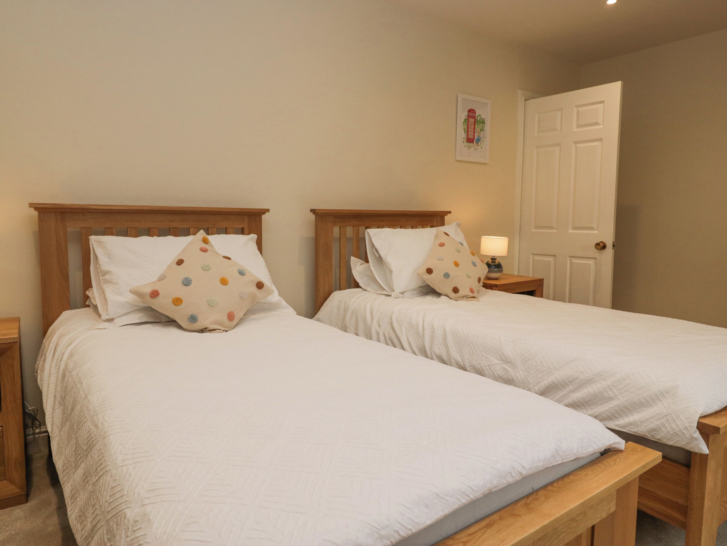 A bedroom with two single beds, wooden headboards, white bedding, and a bedside table with a lamp.