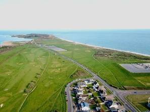 An aerial view of a coastal area with a golf course, a residential neighborhood, and a beach. - Bayview Cottage (Bournemouth)