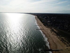 Luchtbeeld van een strand met een lange zandvlakte en een helder uitzicht op de oceaan.