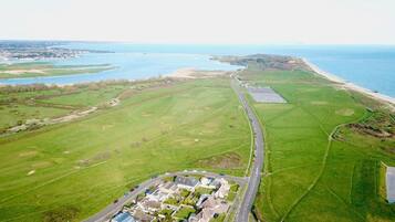 Luchtbeeld van een kustgebied met een weg die leidt naar een groep huizen, een groot veld en een strand.