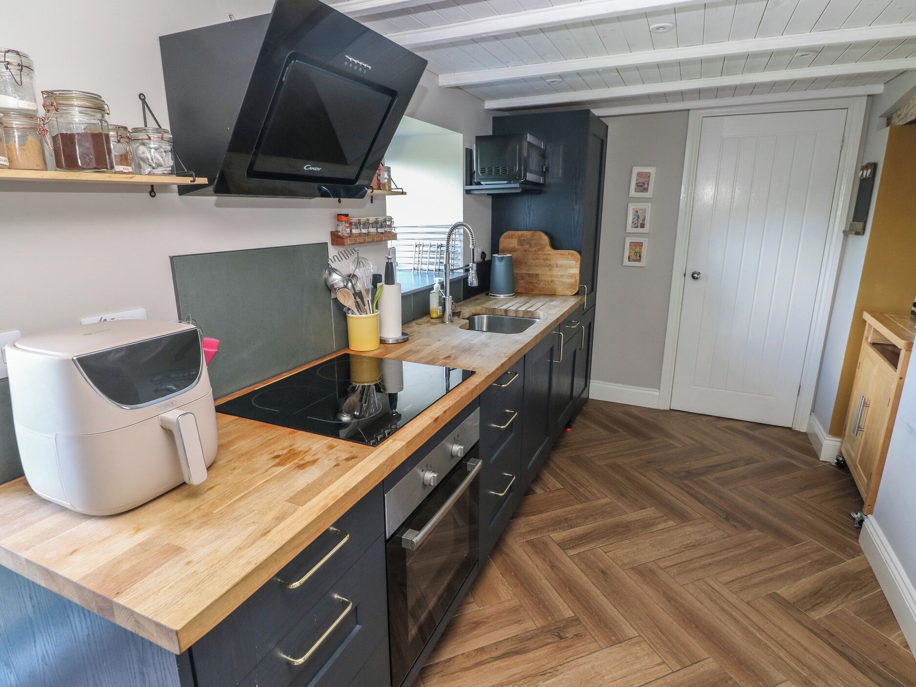 A modern kitchen with a built-in stove, microwave, and oven. There are wooden cabinets, a wooden countertop, and a herringbone-patterned floor.