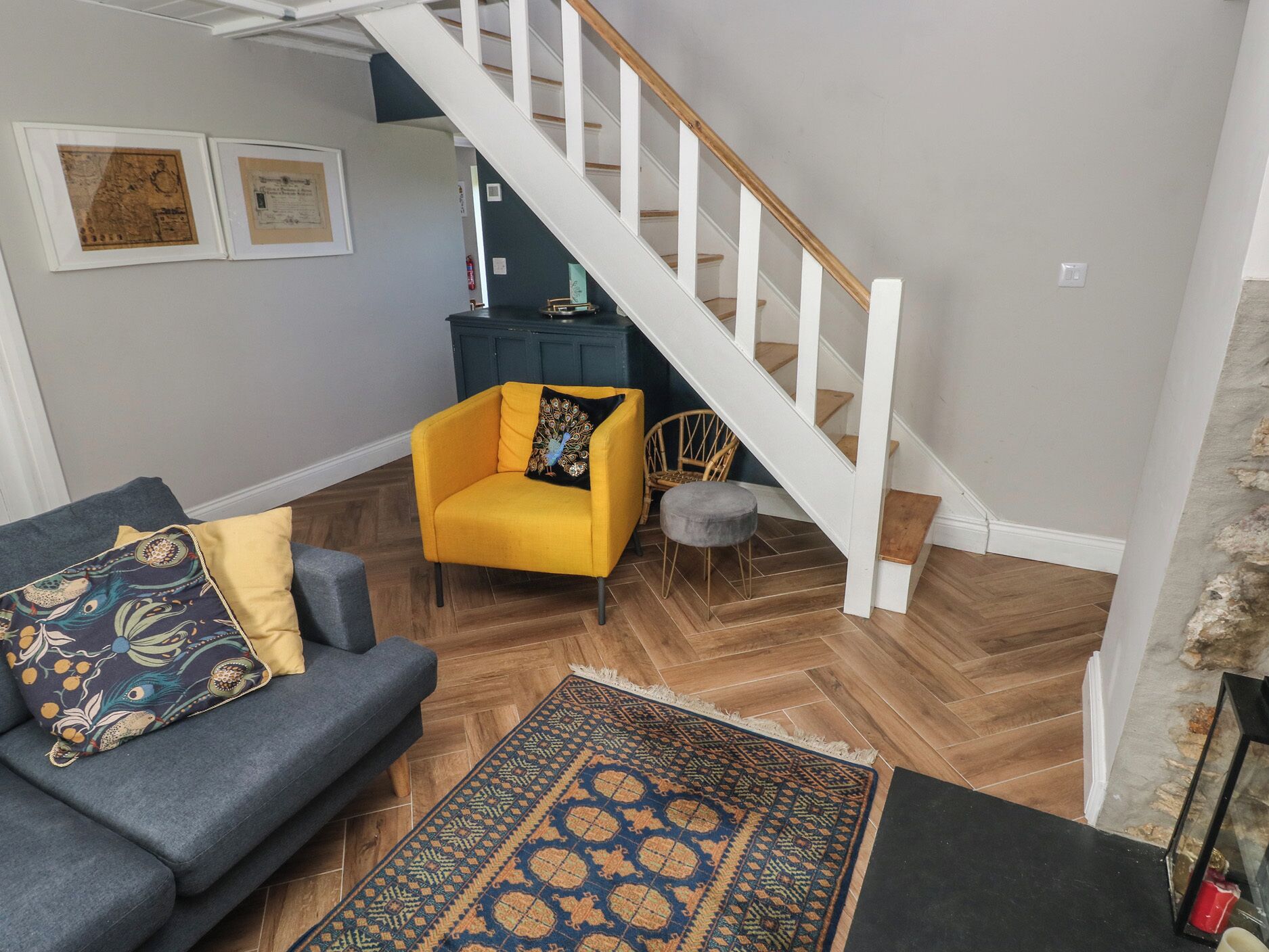 A living room with a sofa, a yellow armchair, a patterned rug, and a staircase.