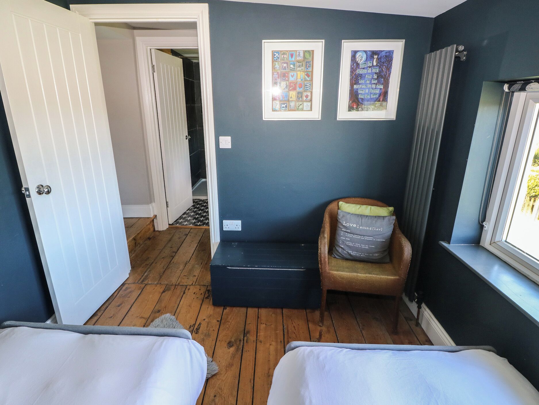 Een kamer met twee bedden, een stoel, een raam en twee ingelijste foto's aan de muur.
