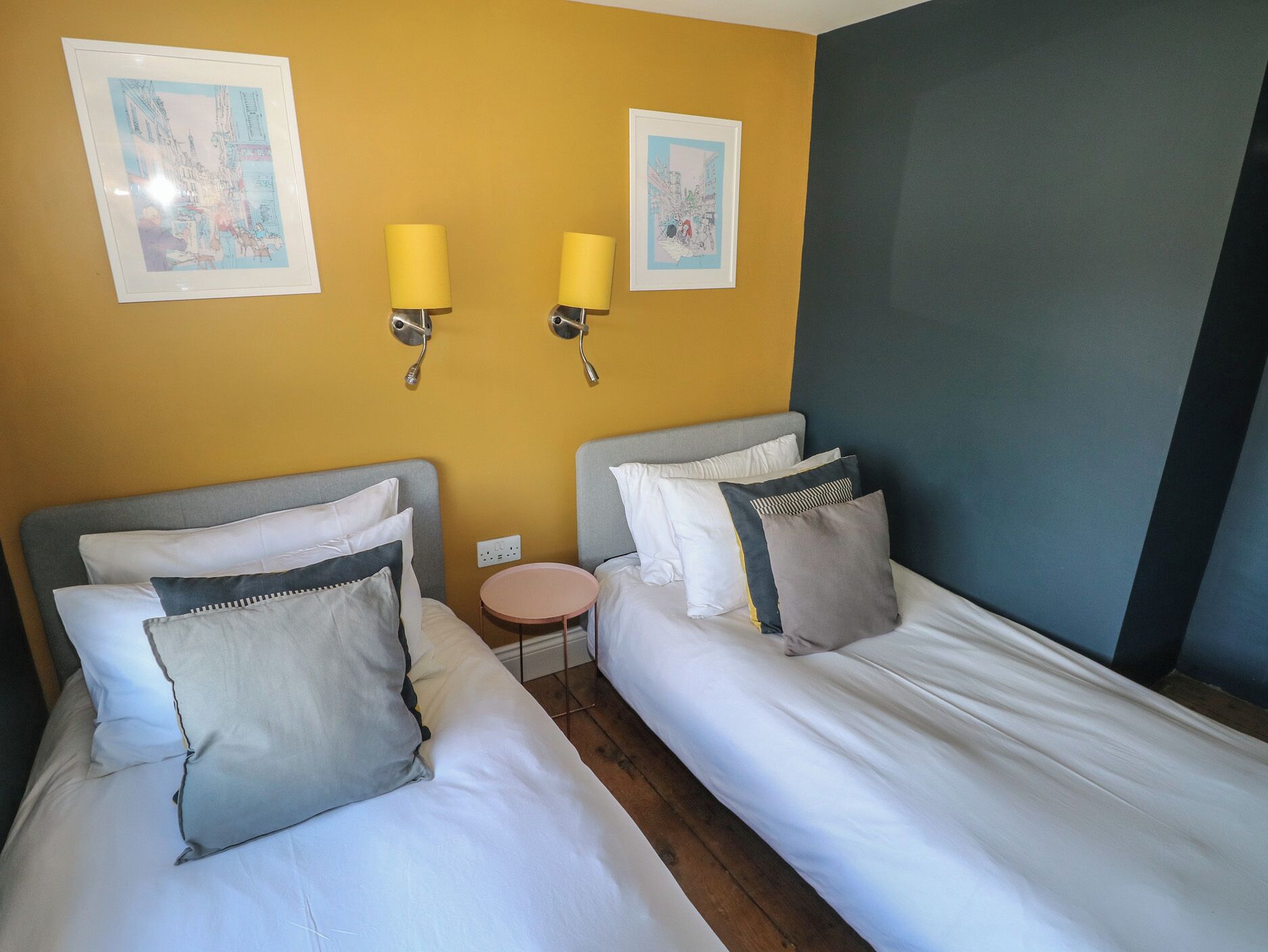 Habitación de hotel con dos camas, una mesita redonda y dos lámparas de pared.