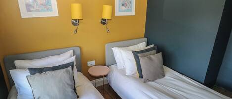 Habitación de hotel con dos camas, una mesita redonda y dos lámparas de pared.