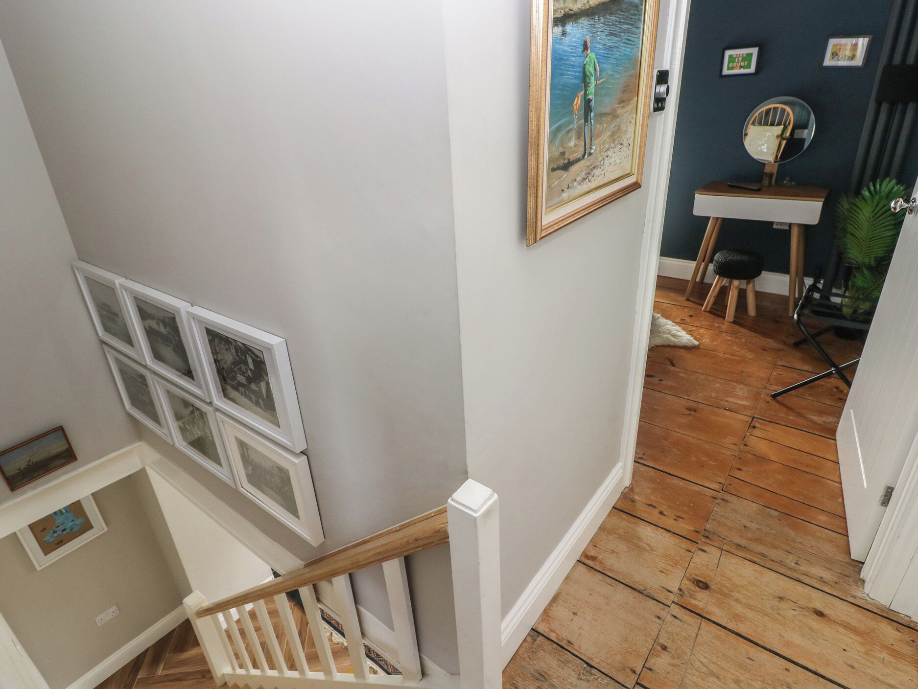 A staircase with a white railing, wooden flooring, and a wall with framed pictures.