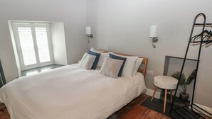 A bedroom with a large bed, two bedside lamps, a small round table, a mirror, and a plant. - Min-y-ffordd (Newport)