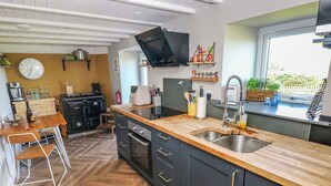 A modern kitchen with a wooden countertop, black cabinets, and a built-in oven. There is a dining area with a table and chairs, and a window providing a view of the outdoors. - Min-y-ffordd (Newport)