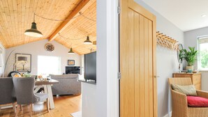 A modern interior with a wooden ceiling, a dining area with chairs, a sofa, and a kitchen area with a TV. - Smugglers (Bodmin)