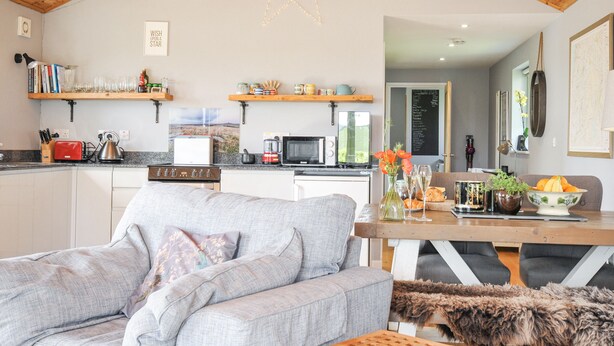 A cozy living room with a grey sofa, a wooden dining table with a vase of flowers, and a fluffy rug. - Smugglers (Bodmin)