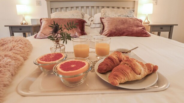 Un plateau de petit-déjeuner bien présenté, avec des demi-pamplemousses, des verres de jus et des croissants, posé sur une table de chevet dans une chambre d’hôtel.
