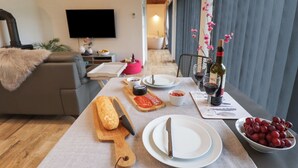 Un coin repas avec une table dressée pour deux personnes, comprenant une miche de pain, un couteau, un bol de raisins et une bouteille de vin.