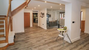 A spacious living area with a wooden staircase, a glass door leading to a kitchen, and a dining area with a high chair. - 85A Braybrooke Road (Kettering)