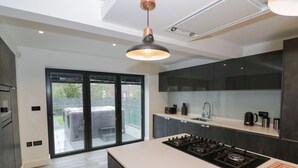 A modern kitchen with dark cabinetry, a central island with a stove, and a large sliding glass door leading to an outdoor patio. - 85A Braybrooke Road (Kettering)
