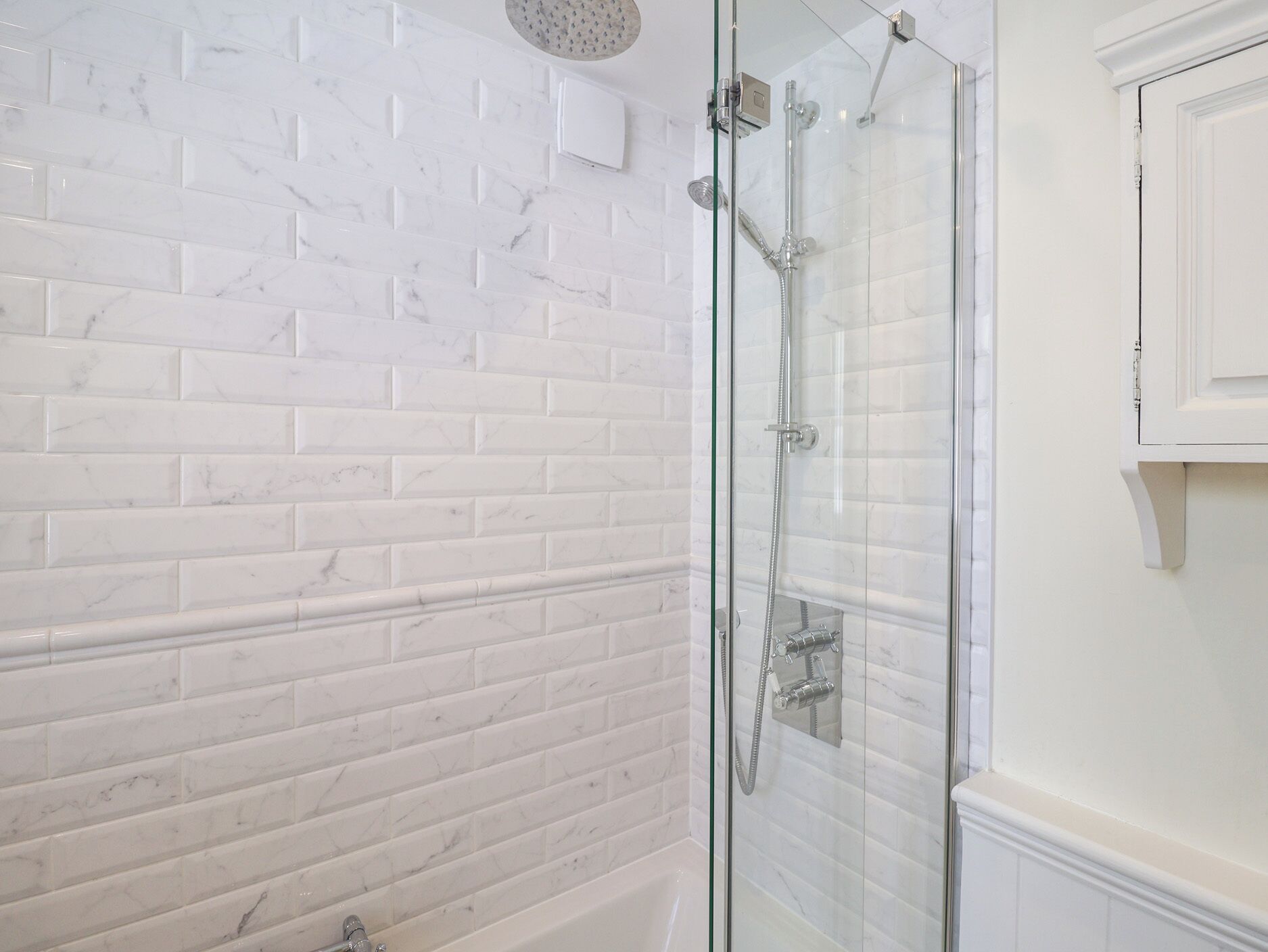 Une salle de bain avec des carreaux de marbre blanc, une douche en verre et un meuble blanc.