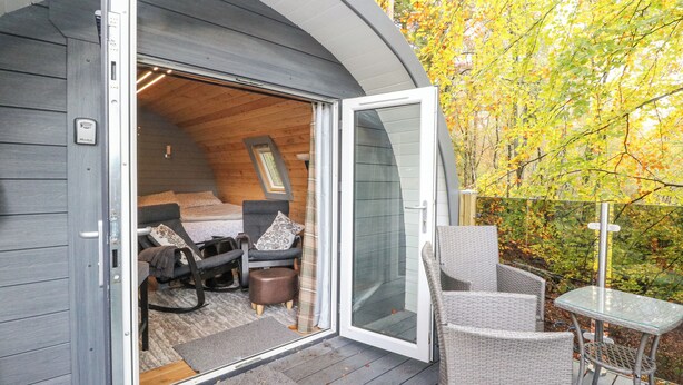 Une cabane chaleureuse avec une chambre à coucher en mezzanine, un petit coin salon et une porte vitrée donnant sur une terrasse.