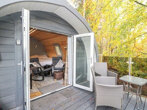 Une cabane chaleureuse avec une chambre à coucher en mezzanine, un petit coin salon et une porte vitrée donnant sur une terrasse.