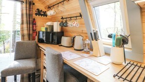 Intérieur d’une cabane en bois comprenant un coin cuisine équipé d’un four à micro-ondes, d’un grille-pain, d’une bouilloire et de tasses suspendues.