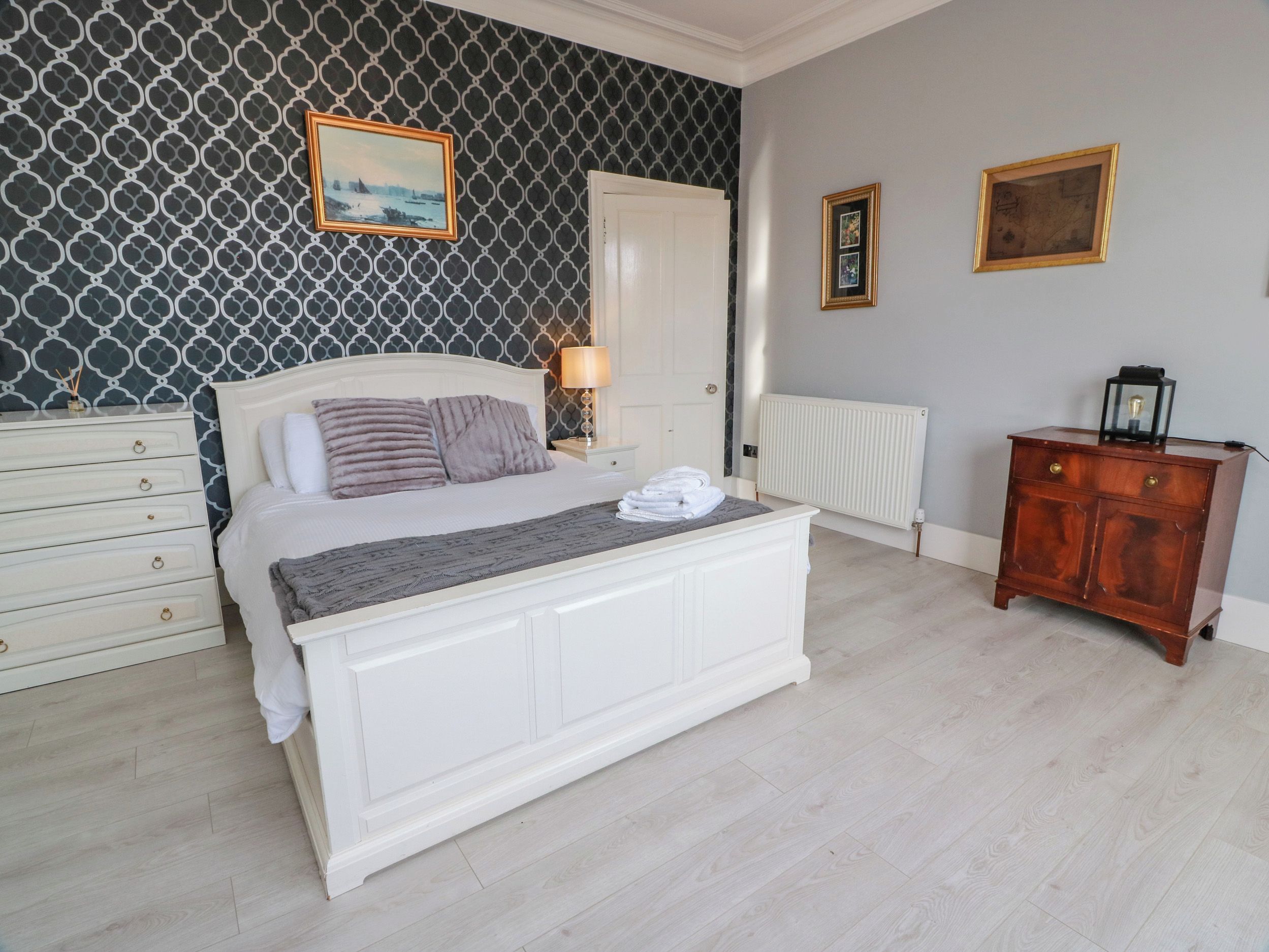 A bedroom with a bed, a dresser, a nightstand, a lamp, and a radiator.
