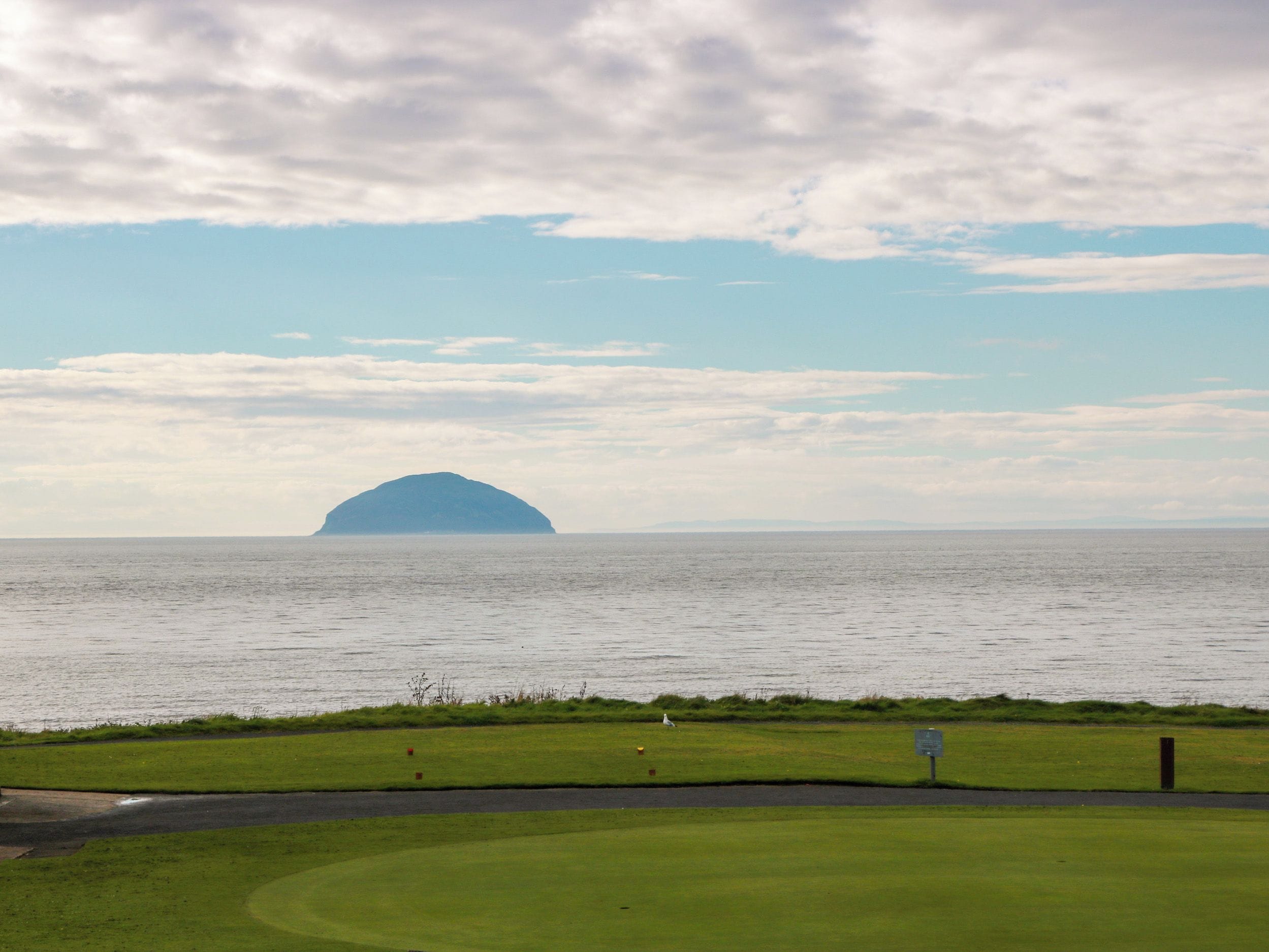 Campo de golfe com um corpo de água e uma ilha ao longe.