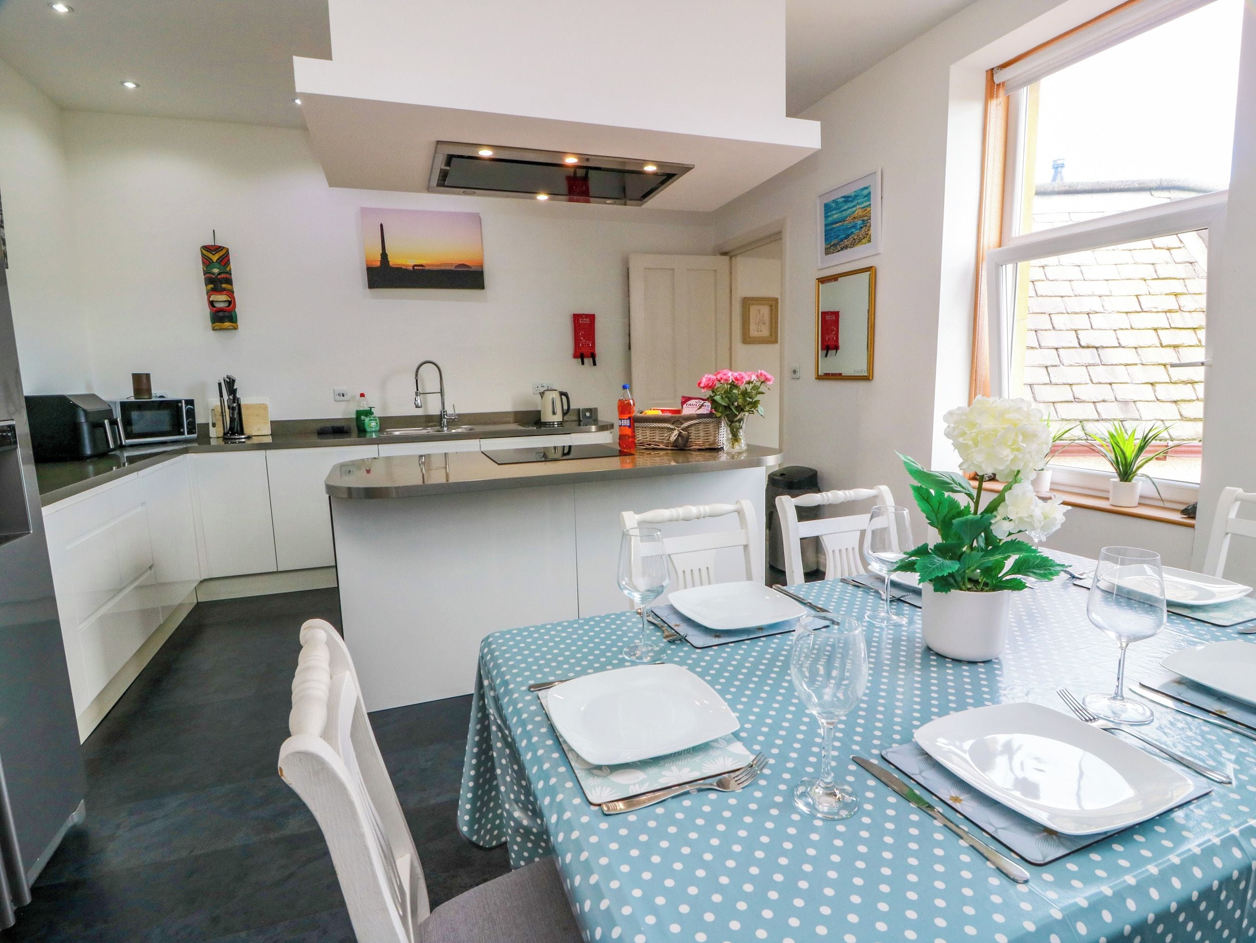 A modern kitchen with a central island, white cabinetry, and a dining area with a blue polka dot tablecloth.