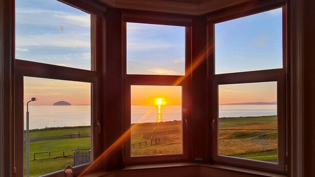 A room with a bay window overlooking a sunset over a beach. - Ailsa View (Girvan)