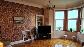A living room with a fireplace, a television, and a view of the outdoors through large windows. - Ailsa View (Girvan)