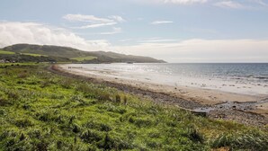 A coastal landscape with a sandy beach, grassy foreground, and hills in the background. - Ailsa View (Girvan)