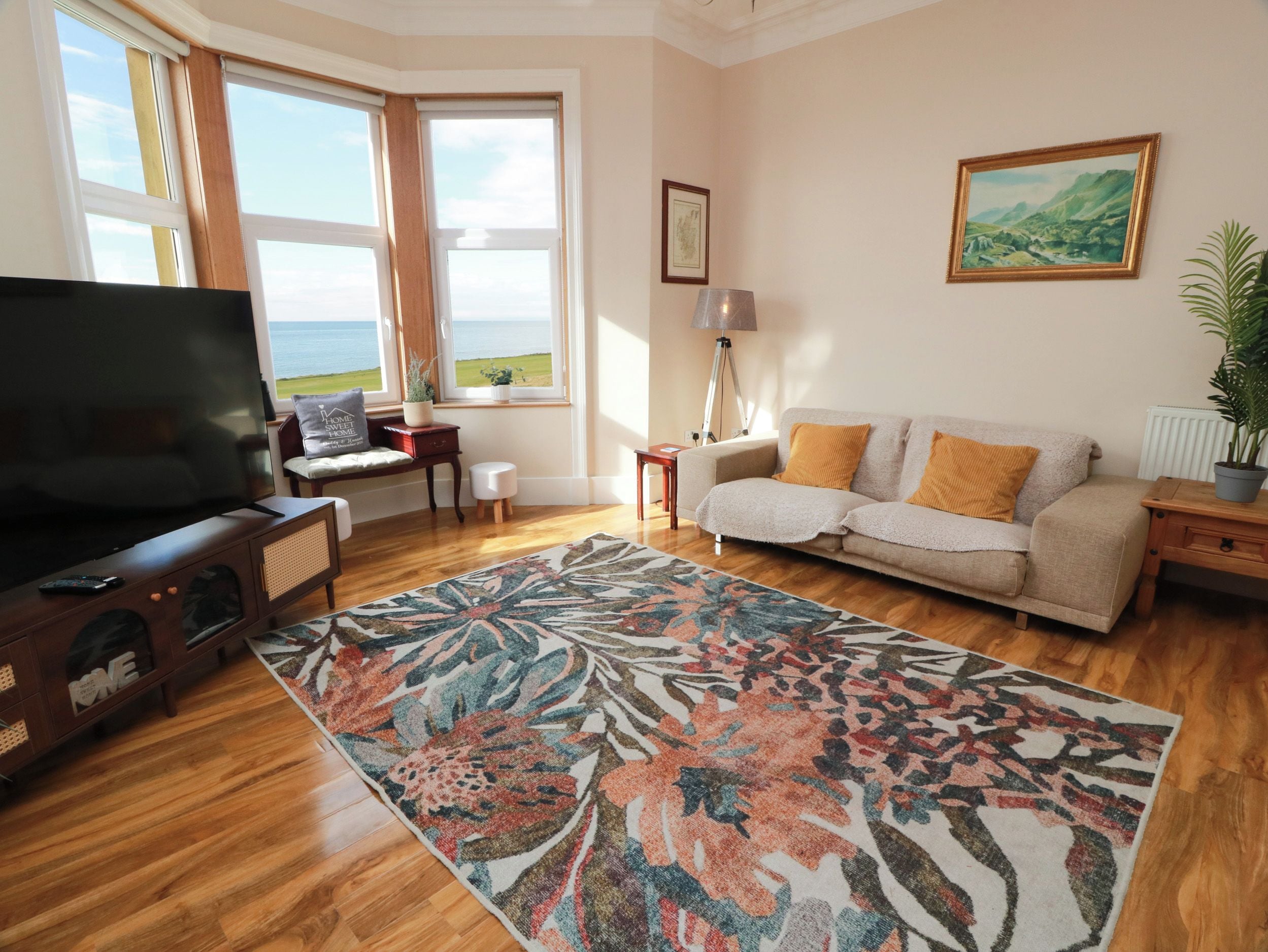 Una sala de estar con un televisor de pantalla plana grande, un sofá, una mesa de centro y vistas al exterior a través de las ventanas.