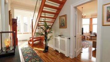 A spacious hallway with a wooden staircase, a decorative rug, and a potted plant.