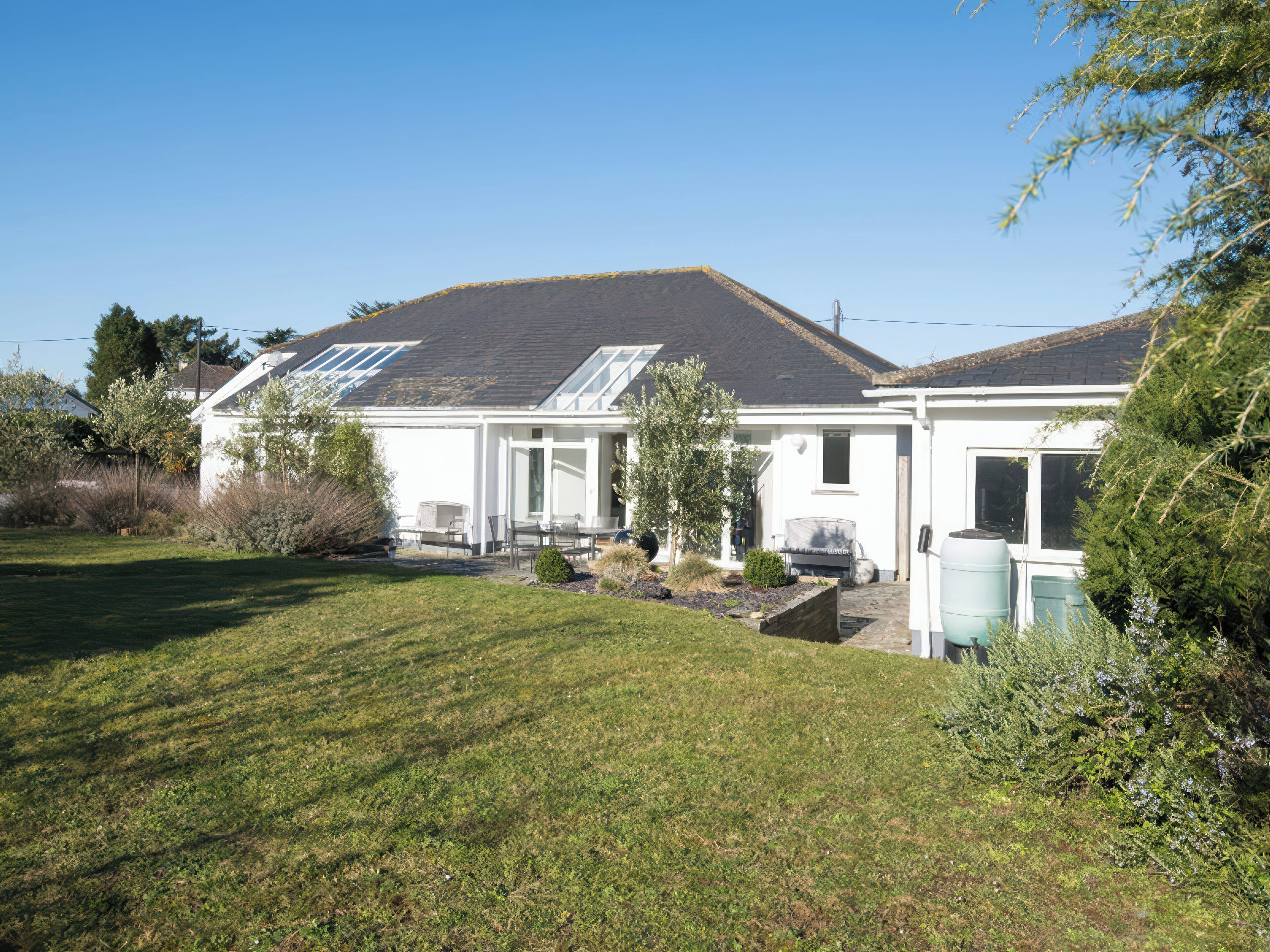 Une maison avec un toit en pente, un porche à l’avant et un petit jardin.