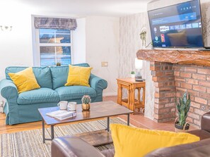 Una sala de estar con un sofá color turquesa, cojines amarillos, una mesa de centro y un televisor instalado en una pared de ladrillo.