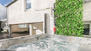 Un bain à remous doté d’un panneau de commande, un bâtiment blanc avec une fenêtre et un mur végétal verdoyant.