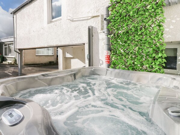 Un bain à remous doté d’un panneau de commande, un bâtiment blanc avec une fenêtre et un mur végétal verdoyant.
