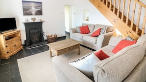 A living room with a fireplace, a wooden TV stand, a sofa set, and a staircase. - Bryn Uchaf (Tyn-y-Gongl)