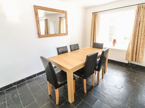 A dining room with a wooden table and black chairs, a mirror on the wall, and a window with curtains. - Bryn Uchaf (Tyn-y-Gongl)