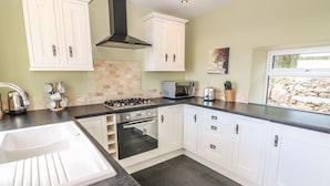 A modern kitchen with white cabinets, a gas stove, a built-in oven, and a large window. - Bryn Uchaf (Tyn-y-Gongl)