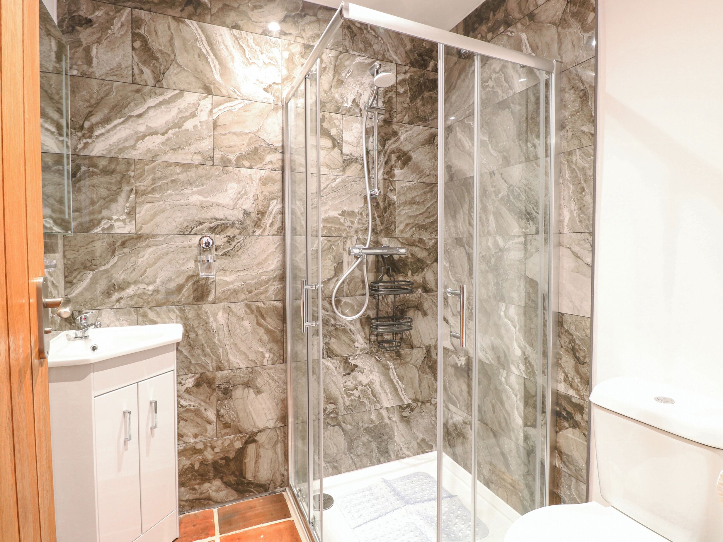 Une salle de bain moderne avec une douche en verre, des murs en marbre et un lavabo blanc.