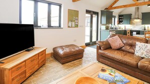 A living room with a television, leather sofa, wooden coffee table, and a kitchen in the background. - The Old Dairy (Dereham)