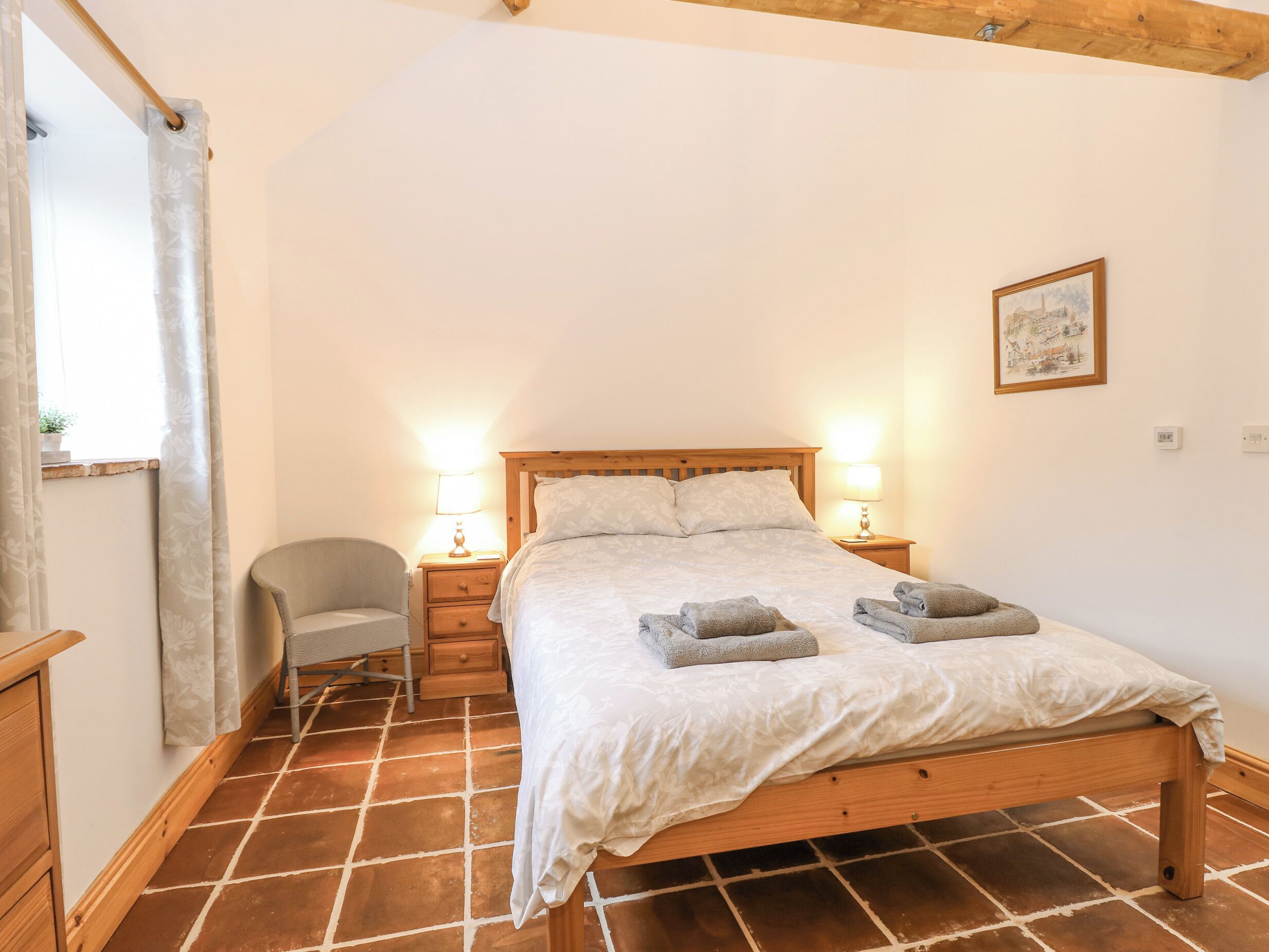 Une chambre à coucher avec un lit en bois, deux tables de chevet avec des lampes, une chaise et une fenêtre avec des rideaux.