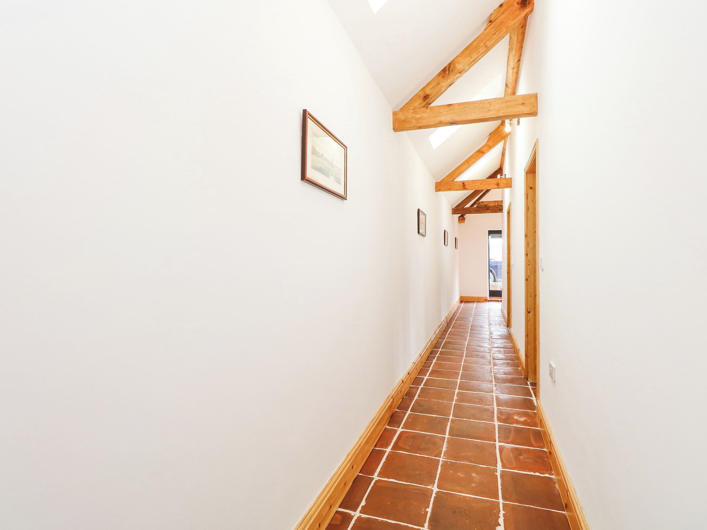 A narrow hallway with white walls, wooden beams, and a tiled floor.