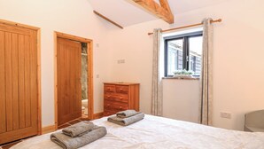 A bedroom with a bed, wooden wardrobe, and a window with curtains. - The Old Dairy (Dereham)