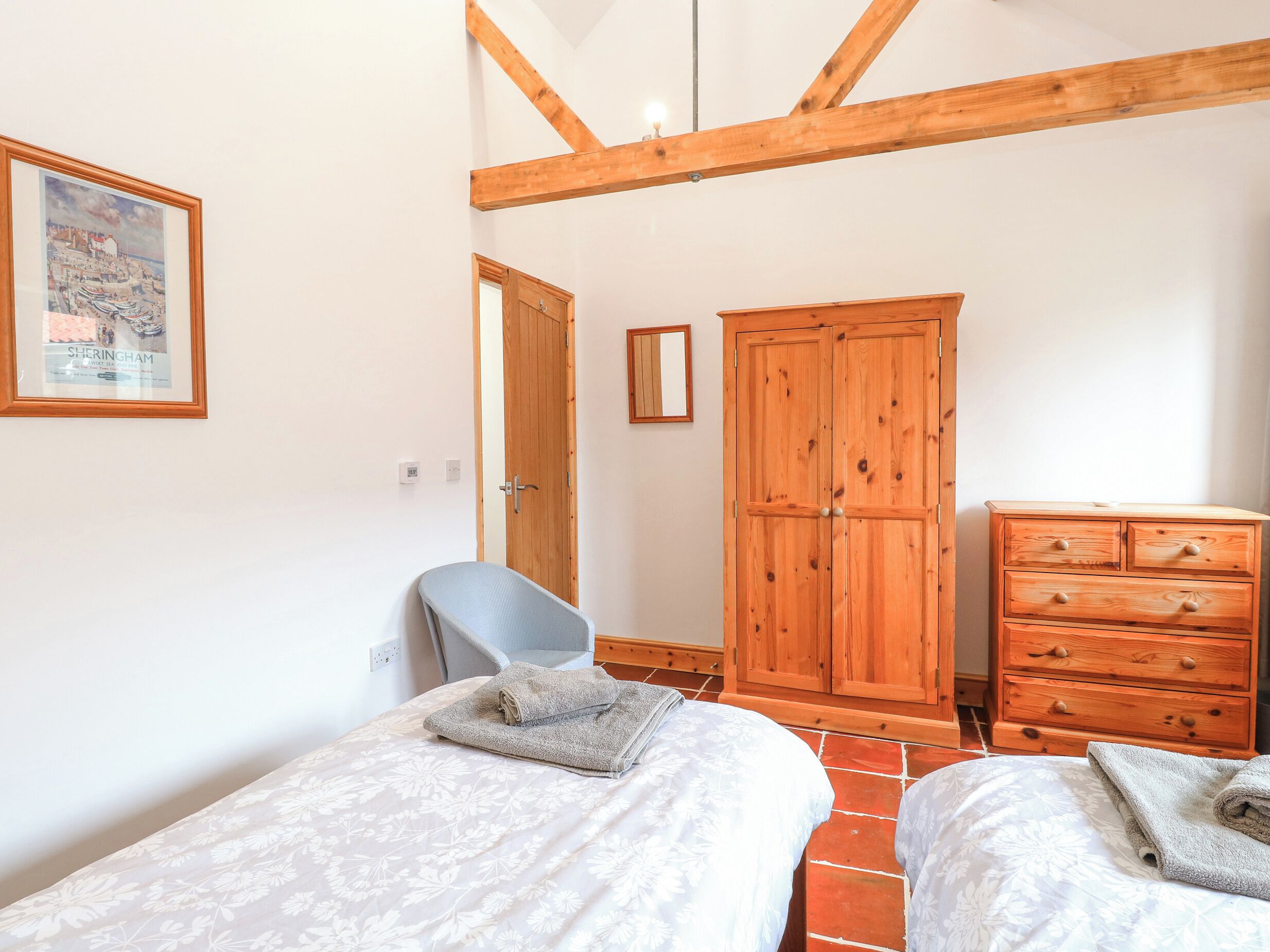 A bedroom with two beds, a wooden wardrobe, a desk, and a chair.