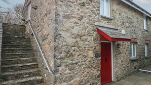 A stone building with a red door and a staircase leading to a landing. - Wood Cottage (Haverfordwest)