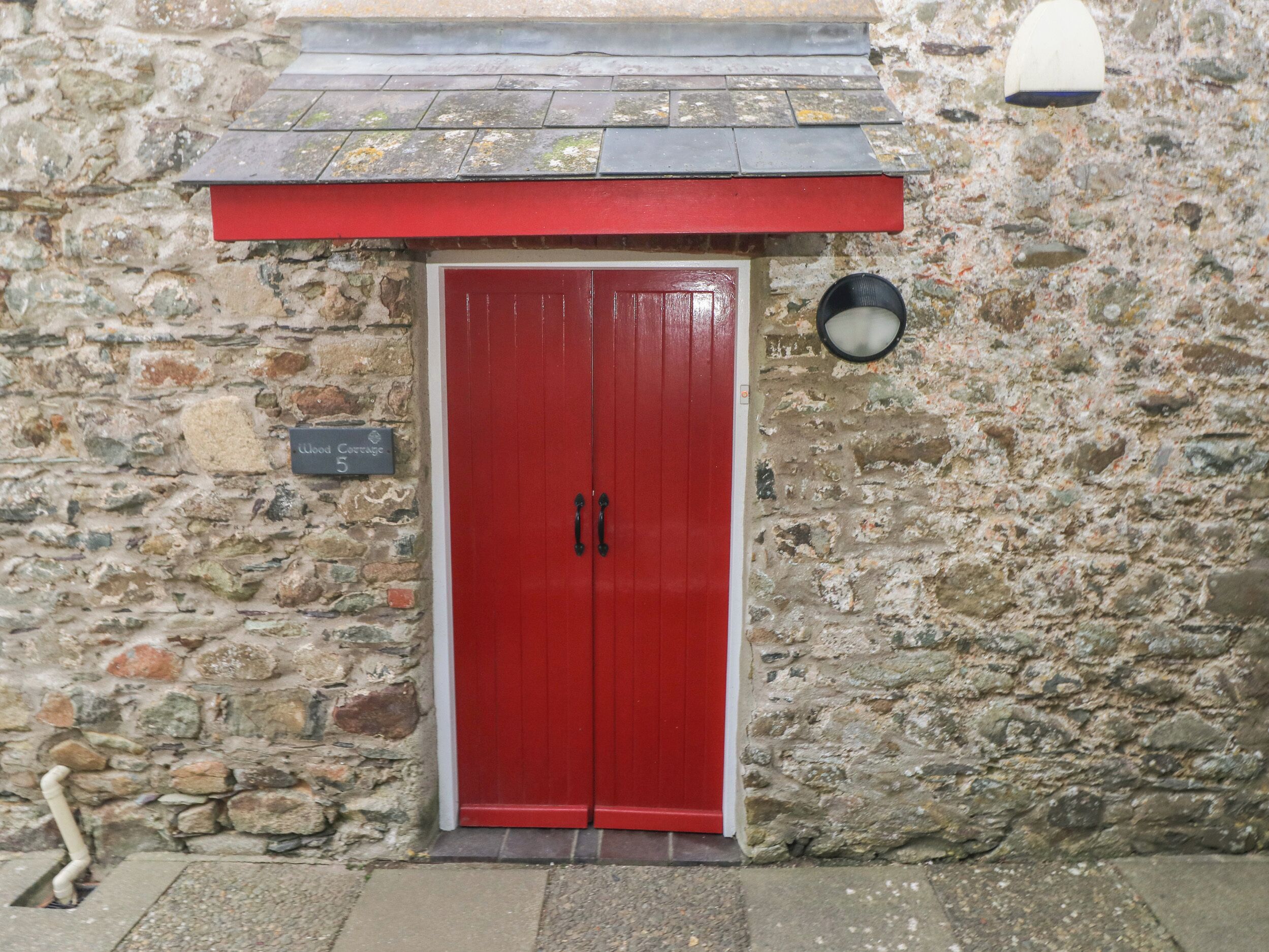 A red door with two handles, set in a stone wall with a weathered roof above.