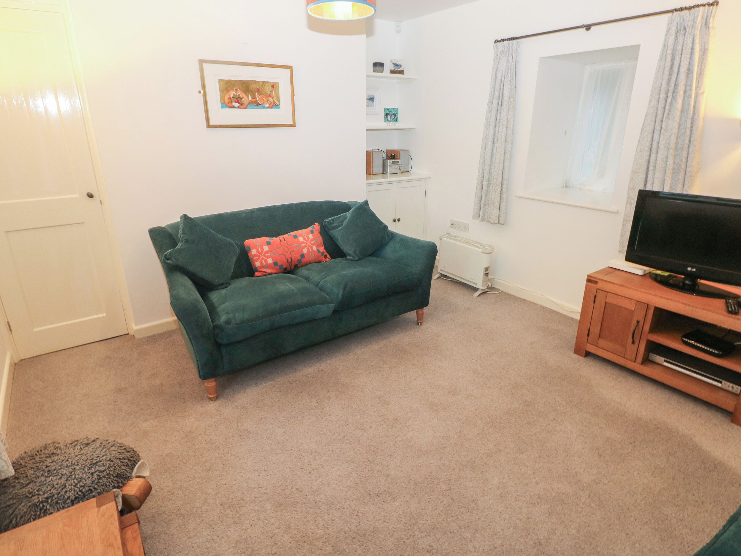 A living room with a green sofa, a television on a wooden stand, a radiator, and a window with curtains.